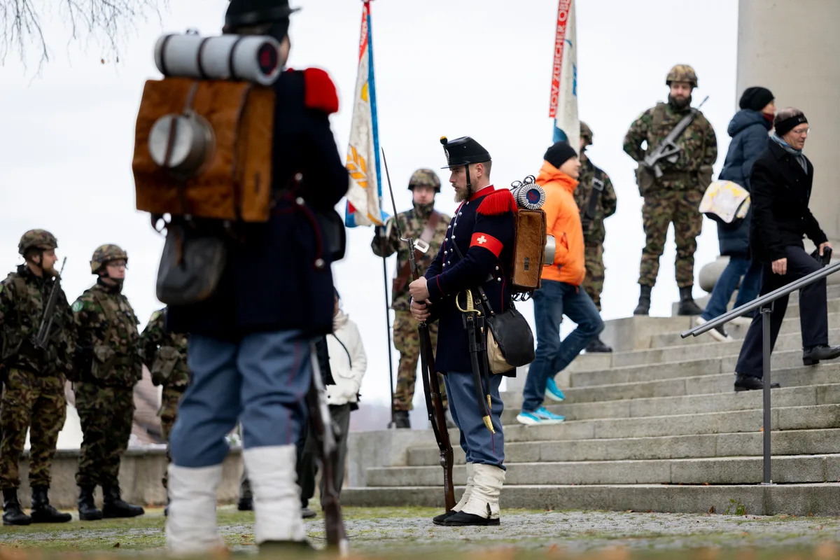 Zeitsprung: Auch einige aktive Unteroffiziere, im Hintergrund im Tarnanzug, stehen Spalier. Man sieht Mitglieder des Unteroffiziersvereins Uster in historischen Uniformen.